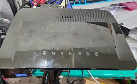 一台黑色 D-Link 網路分享器放置在維修桌面上，指示燈號顯示運作狀態