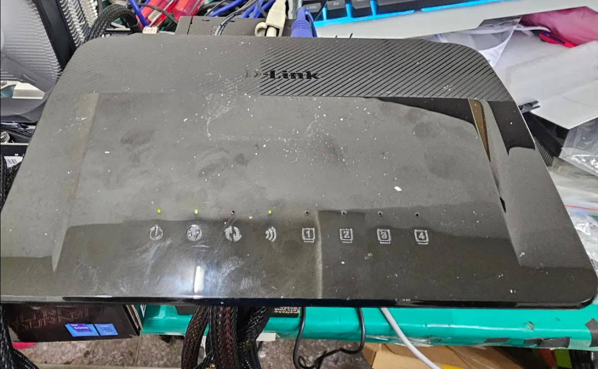 一台黑色 D-Link 網路分享器放置在維修桌面上，指示燈號顯示運作狀態